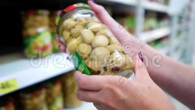 靠近商店货架的白种人女人手在杂货店选择腌蘑菇